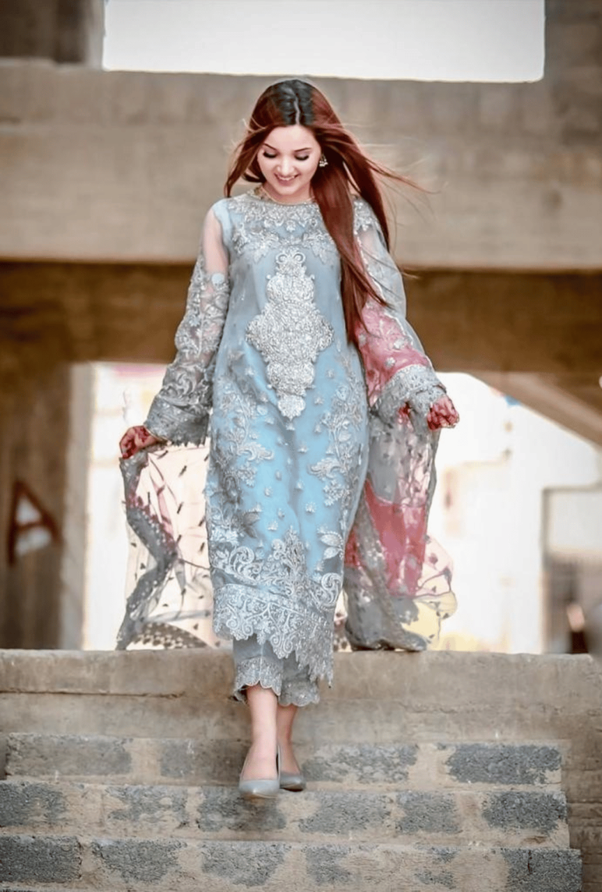 Woman in a light blue and gray embroidered dress walking up stone steps.