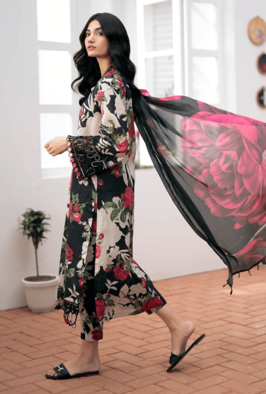 Woman in a floral dress holding a black dupatta with pink roses in a bright room.