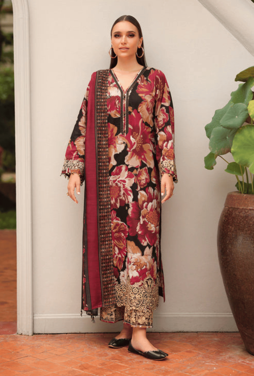 Woman wearing a floral dress with a patterned scarf, standing indoors next to a plant.