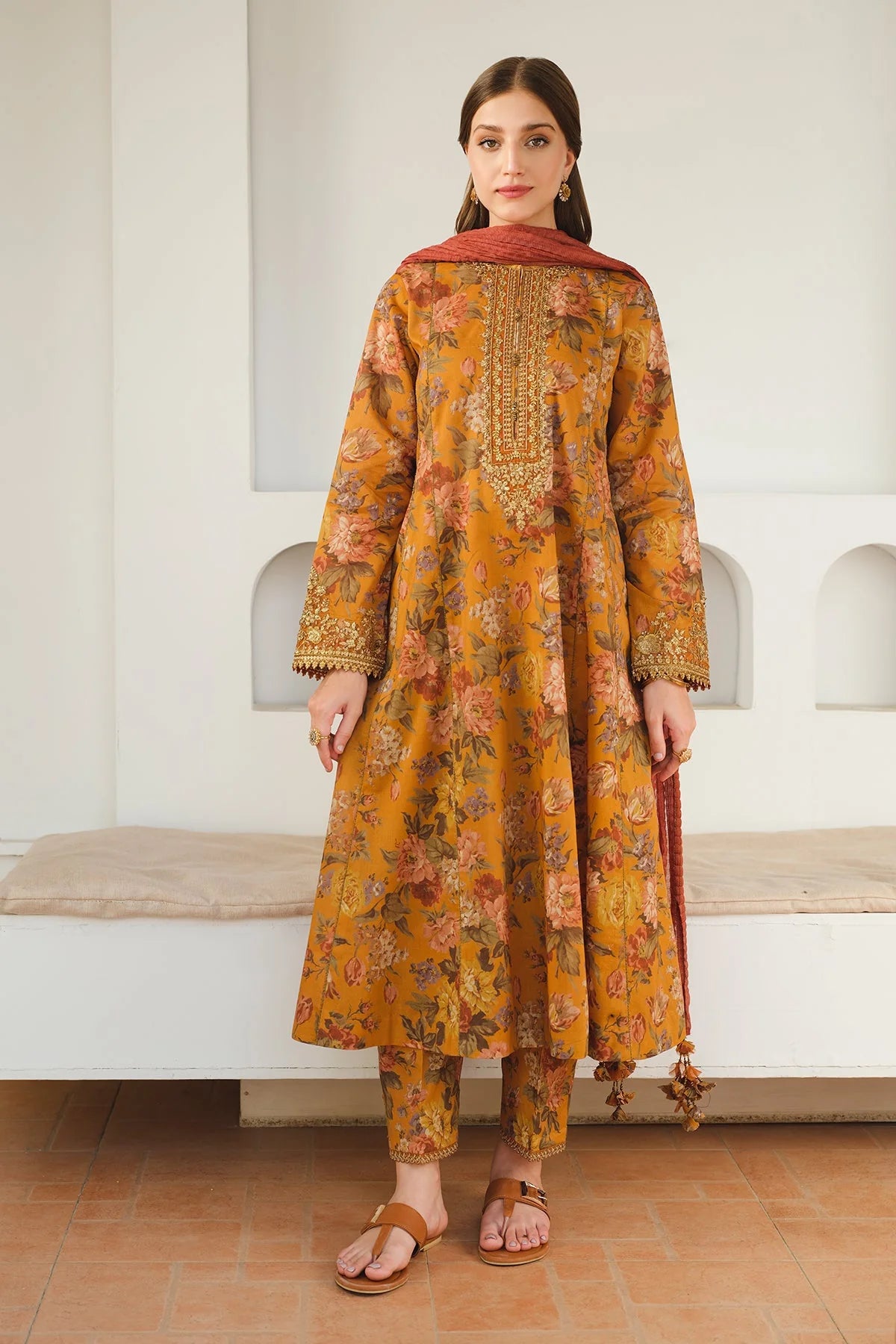 Woman wearing a mustard yellow floral dress with intricate details in an indoor setting.