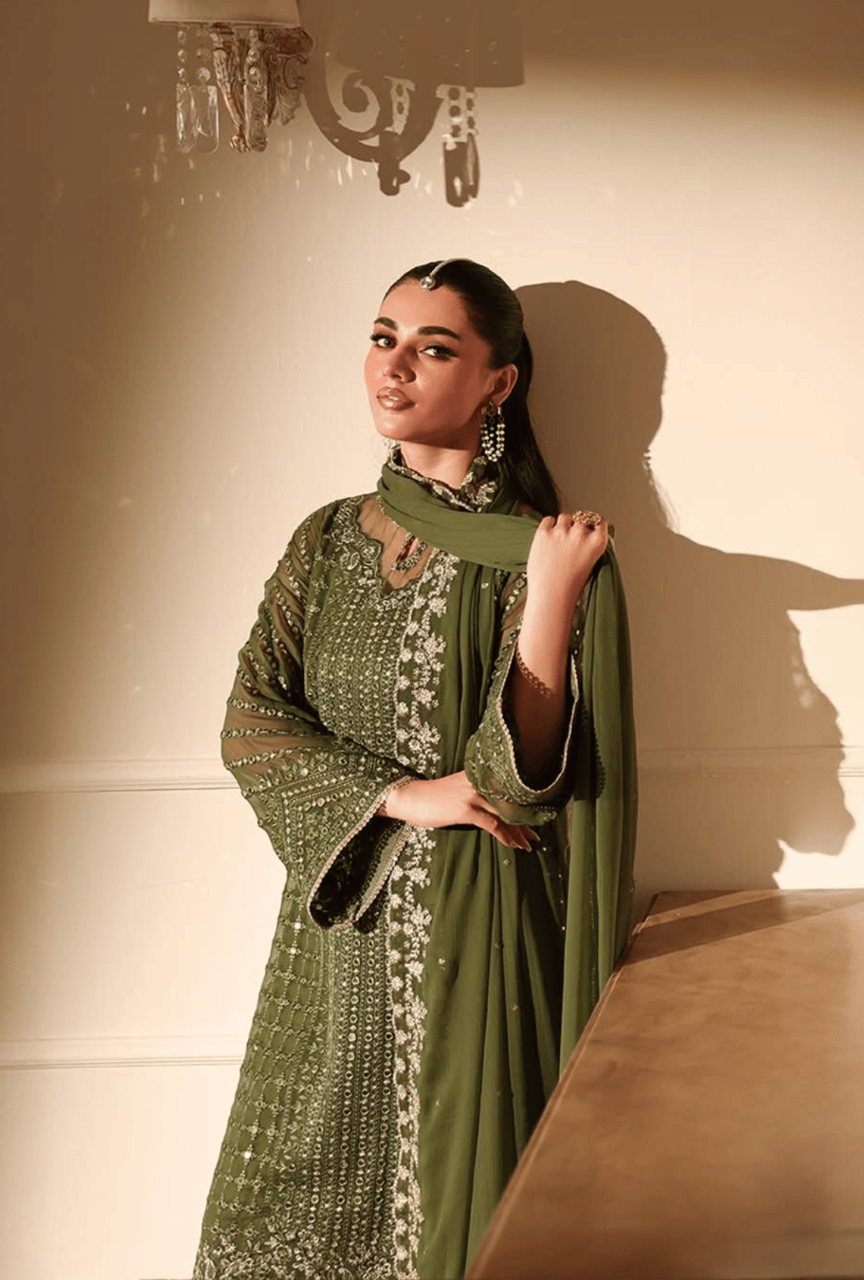 Woman in a green traditional outfit with intricate patterns against a neutral background