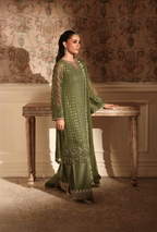 Woman in a green traditional outfit standing in an elegant room with ornate wallpaper.
