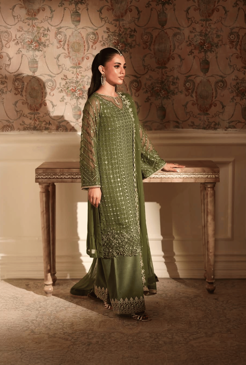Woman in a green traditional outfit standing in an elegant room with ornate wallpaper.