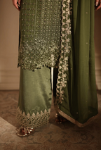 Green traditional outfit with intricate embroidery on a textured floor.