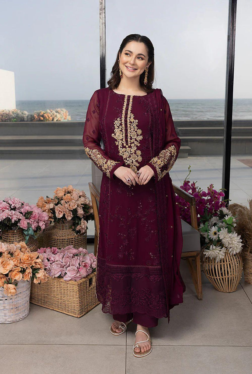 Woman in a burgundy embroidered dress standing in front of a decorative setting with flowers.