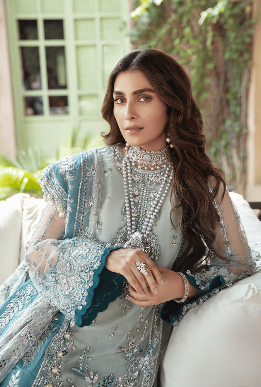 Woman in an ornate traditional outfit with jewelry, sitting on a couch.