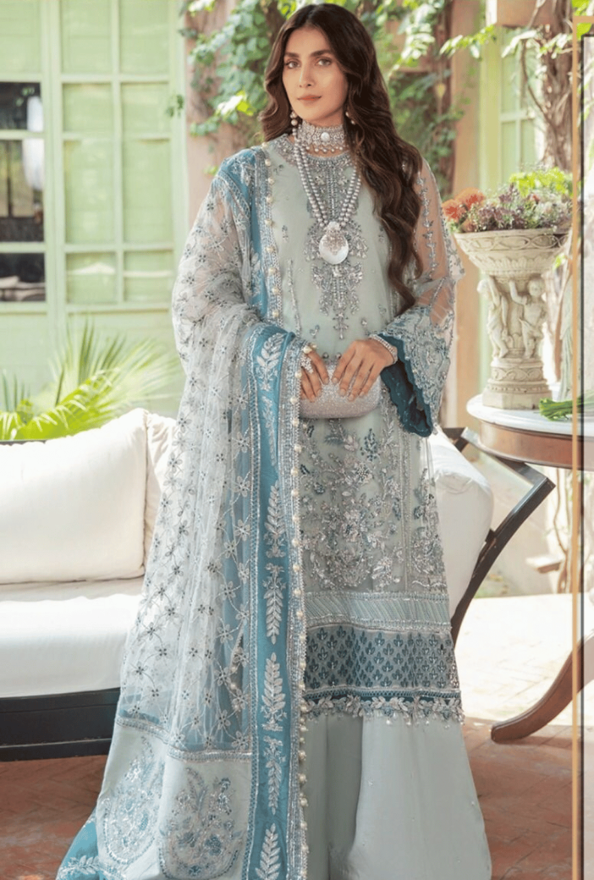 Woman in a light blue and white traditional outfit with intricate patterns in an indoor setting.