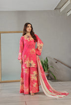 Woman wearing a pink floral outfit with a white dupatta in an indoor setting.
