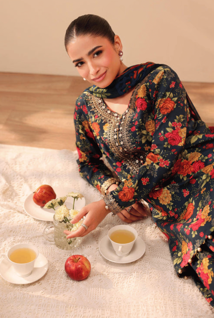 Woman in a floral dress sitting at a table with tea and apples, wearing a ring.