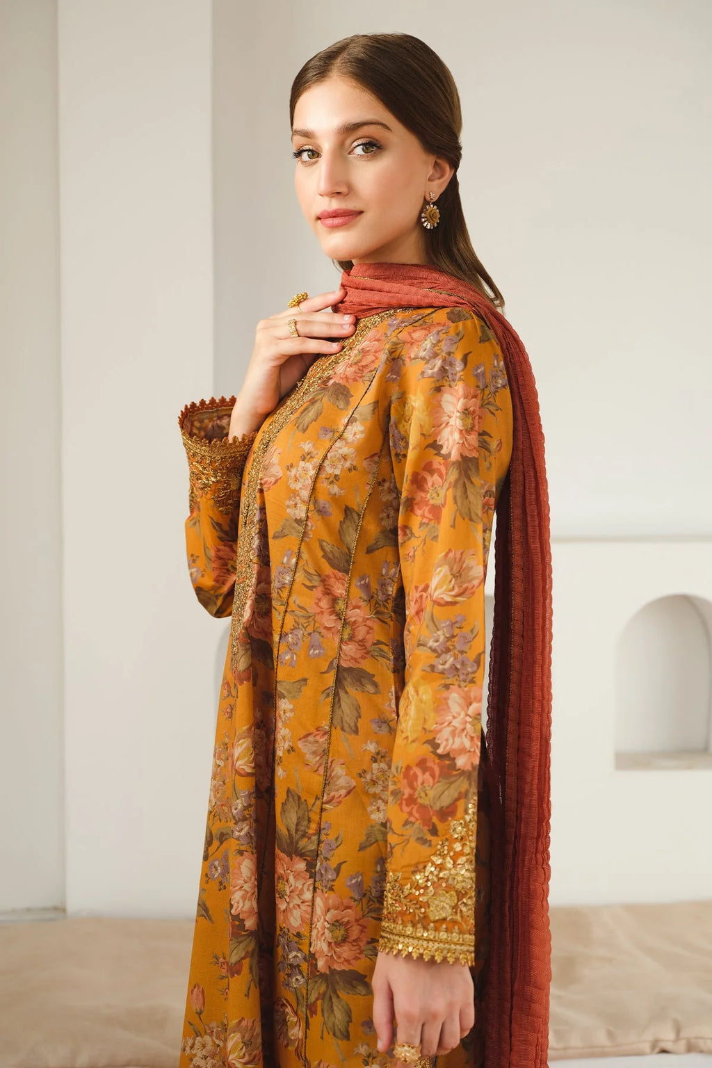 Woman wearing a mustard yellow floral dress with a red dupatta indoors.