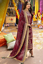 Woman in a traditional maroon and gold embroidered outfit in a festive setting.