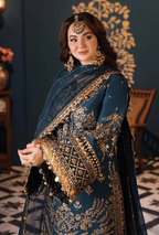 Woman wearing a blue and gold embroidered traditional outfit with jewelry against a dark background.