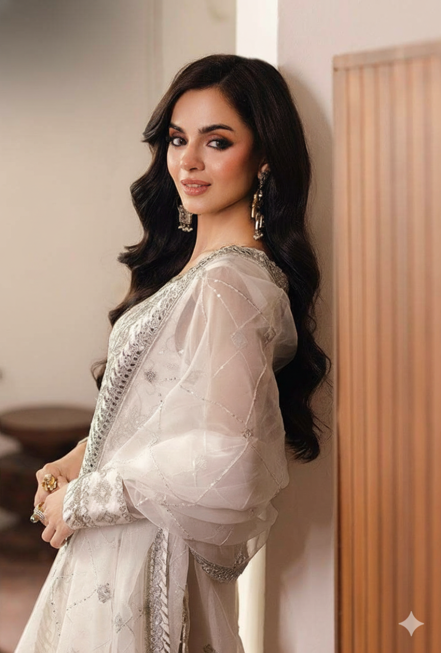 Woman in a white traditional outfit with silver details leaning against a wall.