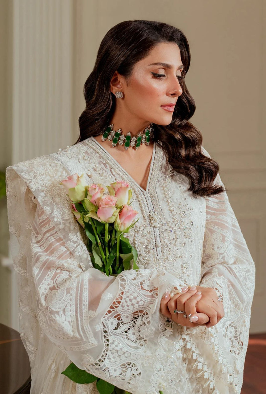 Woman in a white lace outfit holding pink roses indoors