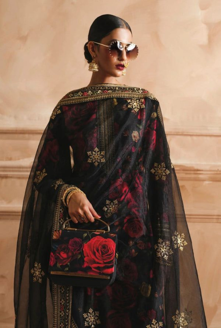 Woman wearing a black embroidered saree with a floral handbag against a beige wall.