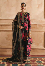 Woman wearing a black and red floral saree with a matching blouse against a beige wall.