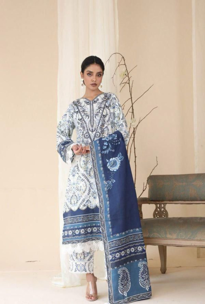 Woman wearing a blue and white embroidered outfit with a matching scarf, standing against a beige curtain.