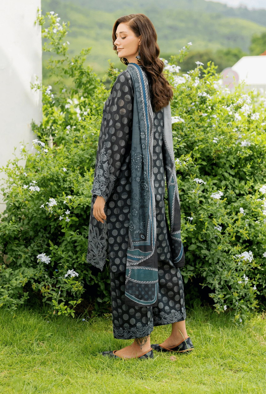 Woman wearing a long, patterned dress standing in a garden with greenery and flowers.