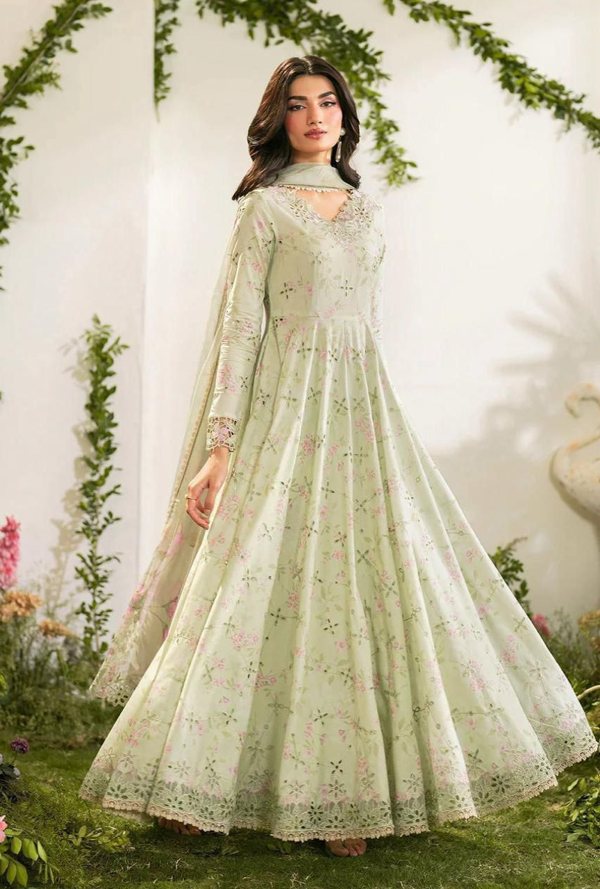 Woman in a light green embroidered dress standing in a decorative setting with flowers and greenery.