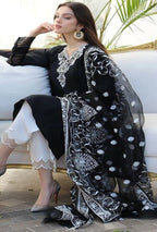 Woman wearing a black and white embroidered traditional outfit sitting on a couch.
