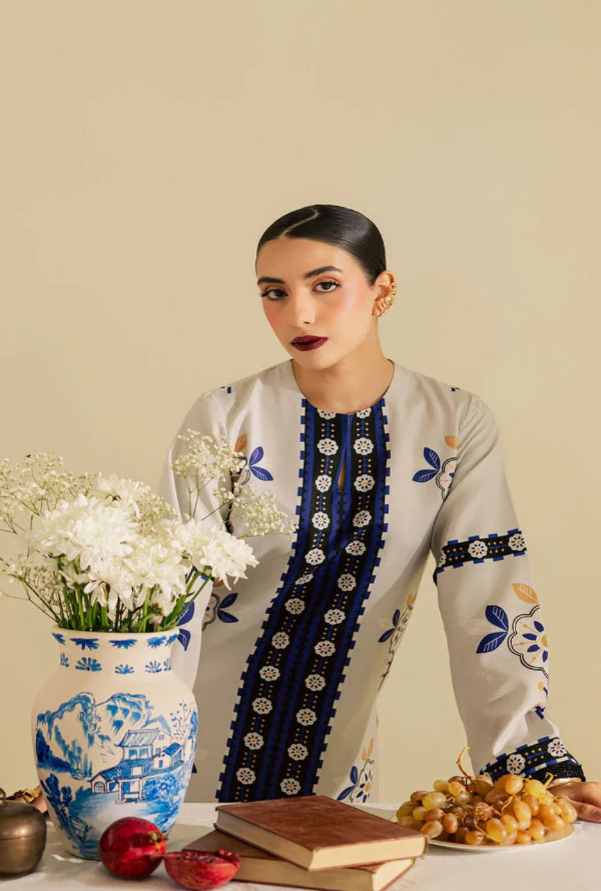Woman wearing a traditional outfit with floral patterns, sitting at a table with decorative items.