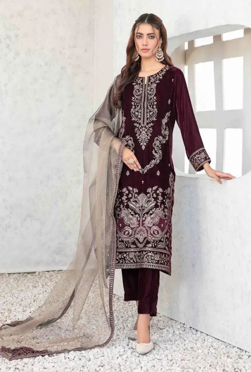 Woman wearing a dark red embroidered outfit with a beige dupatta against a white wall.