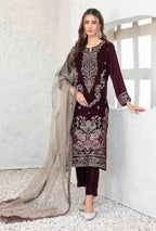 Woman wearing a dark red embroidered outfit with a beige dupatta against a white wall.