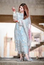 Woman in a light blue embroidered outfit holding a decorative item, standing on a concrete surface with a blurred background.