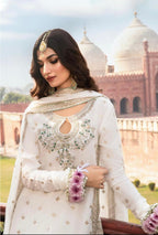 Woman in traditional white embroidered outfit with floral accessories, standing in front of a domed building.