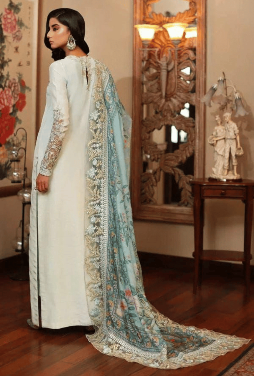 Woman in a traditional outfit with a long, embroidered scarf in a decorated room.