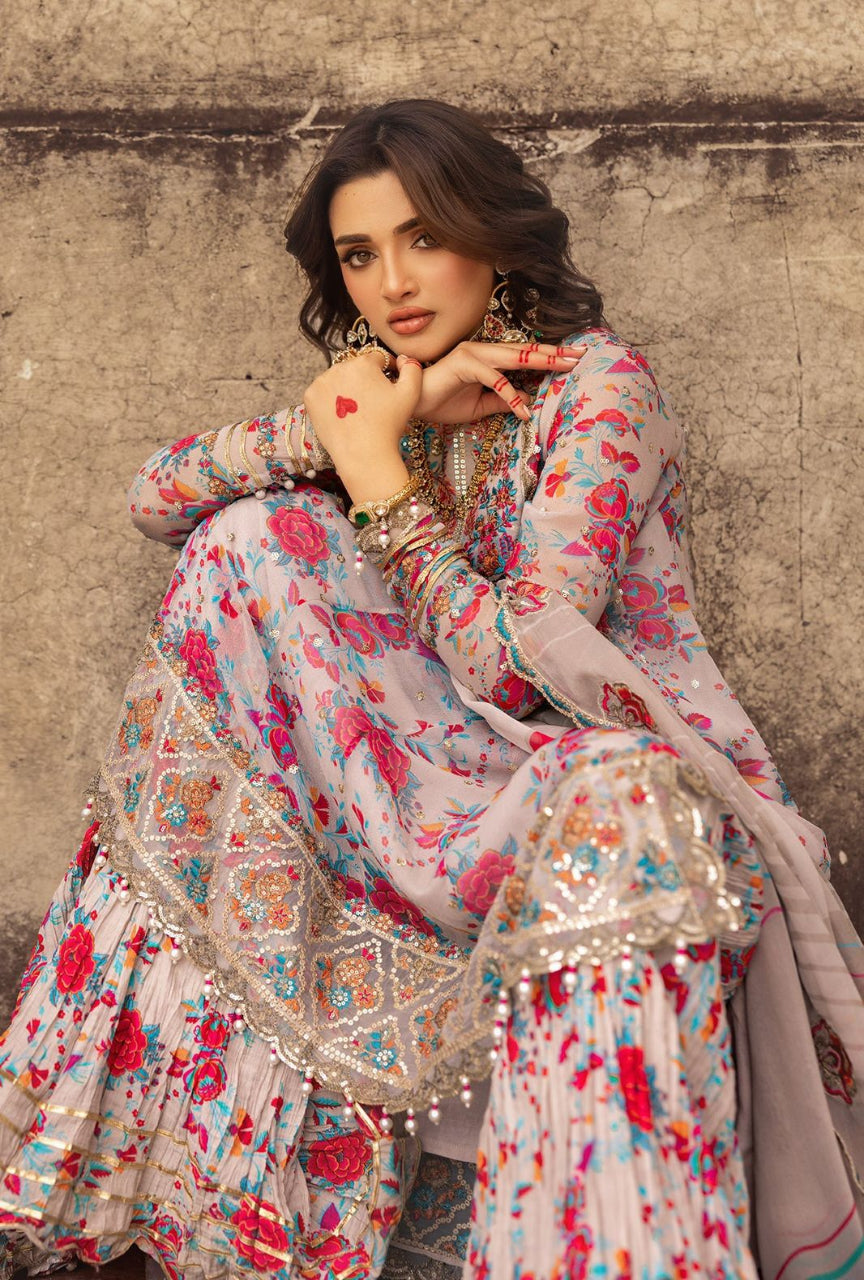 Woman in a floral traditional outfit sitting against a textured wall.