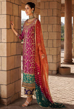 Woman in traditional embroidered outfit standing against a stone wall.