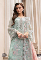 Woman wearing a light blue embroidered dress with pink accents in an elegant interior setting.
