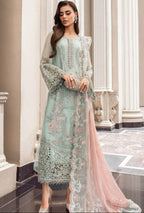 Woman wearing a light green embroidered dress with a pink dupatta in an elegant interior setting.