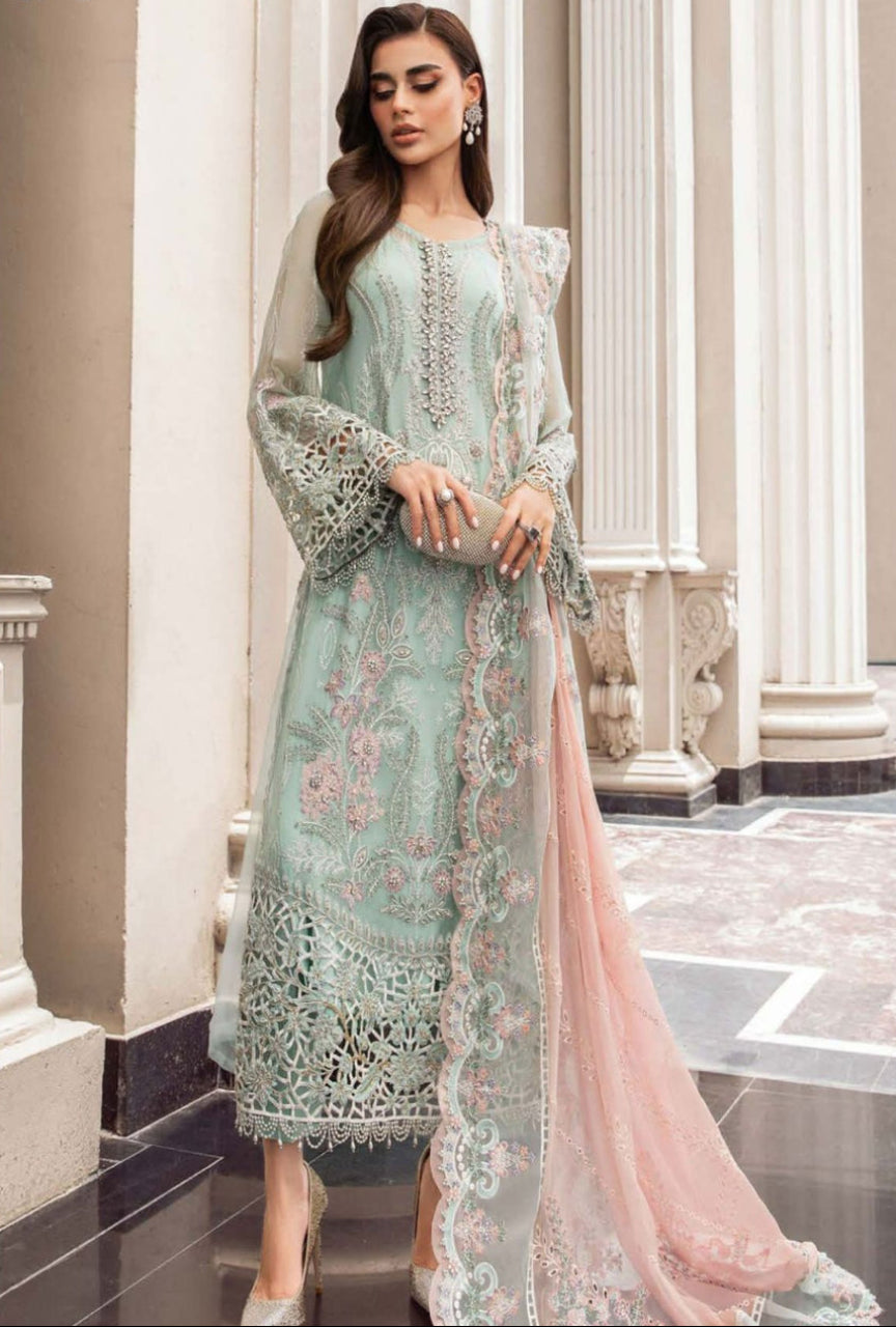 Woman wearing a light green embroidered dress with a pink dupatta in an elegant interior setting.