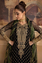 Woman wearing a black embroidered dress with gold detailing and a green dupatta.