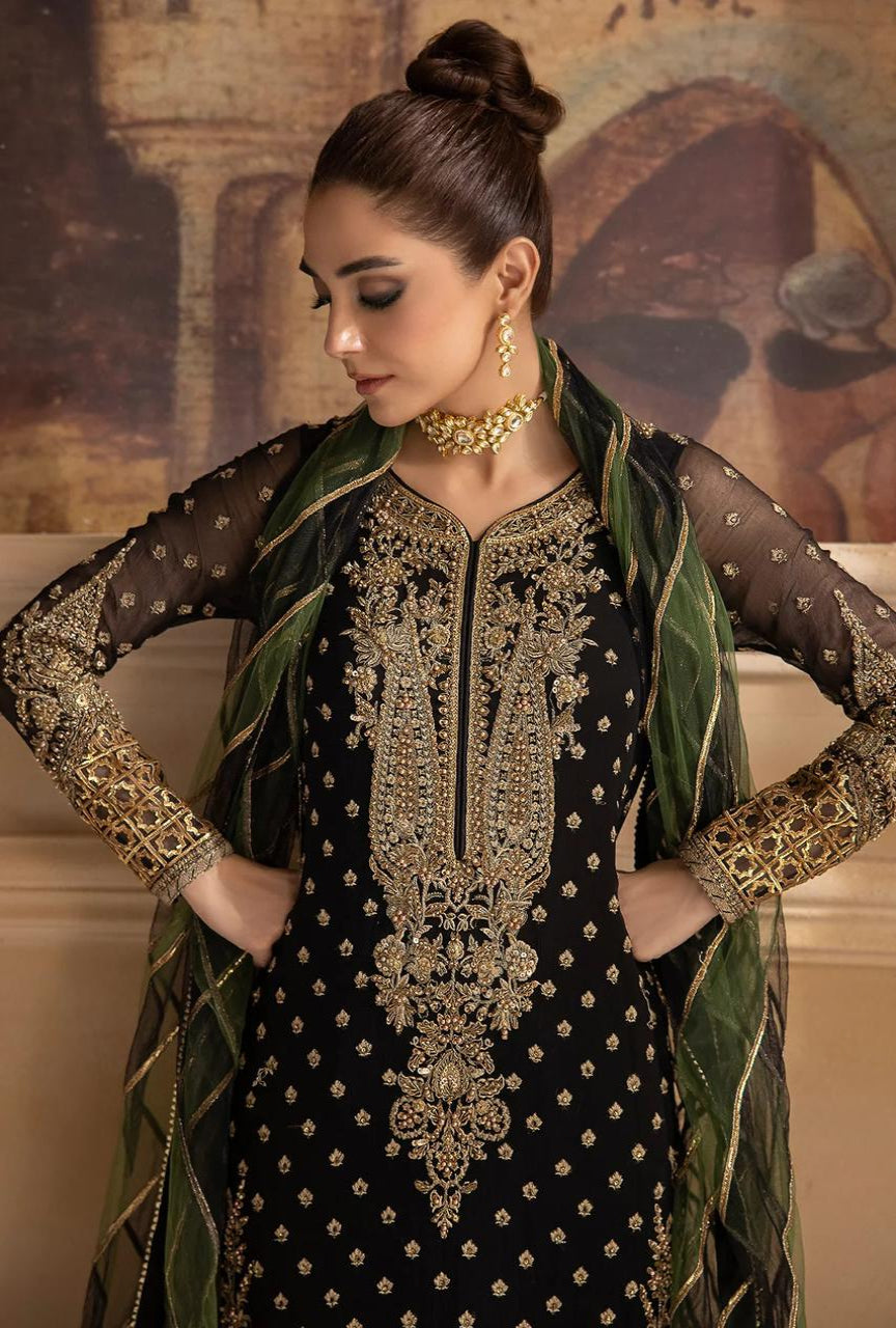 Woman wearing a black embroidered dress with gold detailing and a green dupatta.
