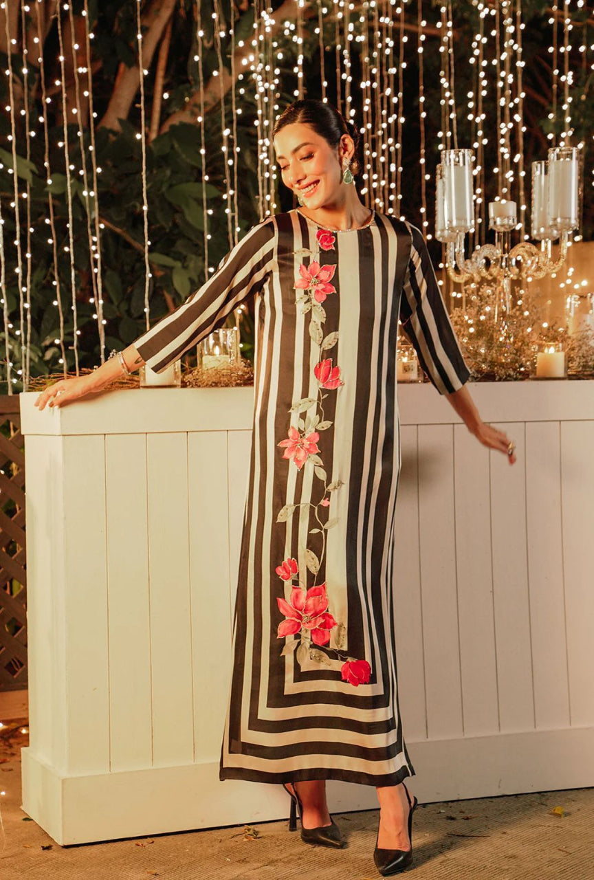 Woman wearing a black and white striped dress with floral patterns standing in front of string lights.