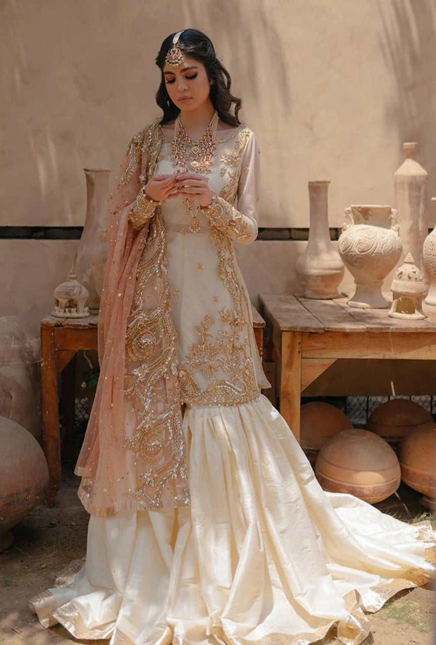 Woman in a traditional outfit with intricate designs standing in a rustic setting.