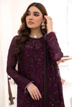 Woman wearing a dark purple embroidered outfit with jewelry against a white background