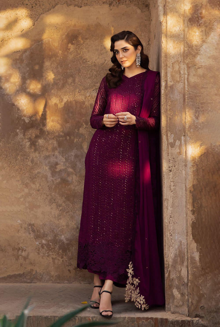 Woman in a dark purple traditional outfit standing against a textured wall.