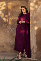 Woman in a dark purple traditional outfit standing against a textured wall.