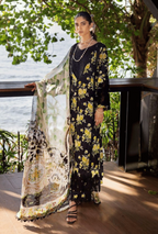 Woman in a floral dress holding a matching shawl by a waterfront.