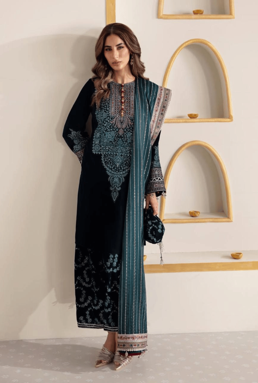 Woman wearing a black and blue embroidered dress with a white wall and shelves in the background
