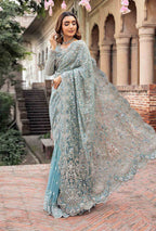 Woman in a light blue saree with floral decorations outdoors.