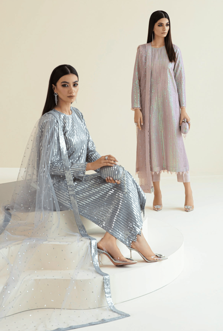 Two women in elegant outfits standing against a white background