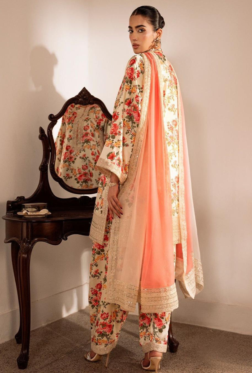 Woman in traditional floral outfit with a pink dupatta standing next to a wooden chair.