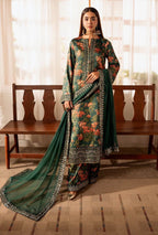 Woman wearing a green floral dress with a dupatta in a room with a wooden bench and white curtains.