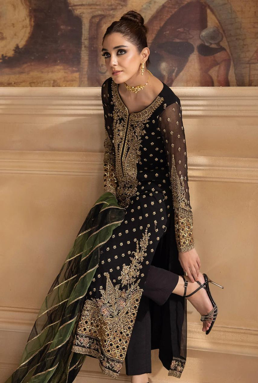 Woman in a black and gold embroidered outfit standing against a decorative wall.