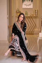 Woman in a black and white embroidered traditional outfit in an elegant interior setting.
